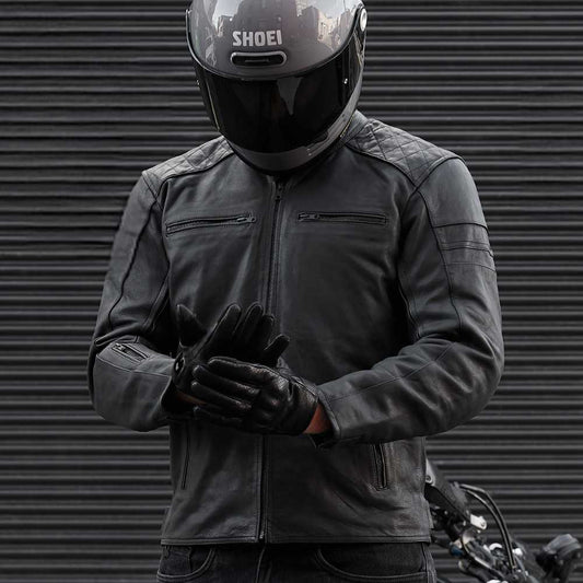 Person wearing a black motorcycle jacket, gloves, and helmet with 'Shoei' branding against a metallic background.