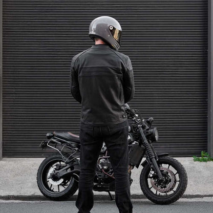 Person wearing a helmet and dark clothing standing next to a motorcycle against a dark background