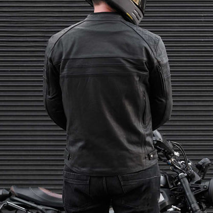 Person wearing a black motorcycle jacket standing next to a motorcycle with a dark background